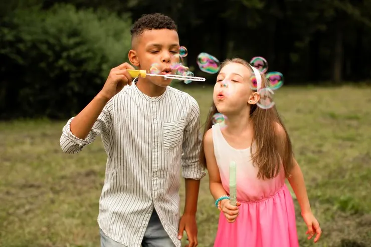 A boy and a girl blowing soap bubbles outside on the grass