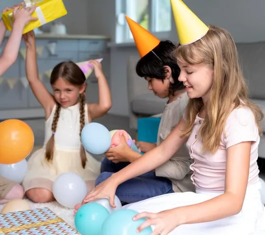 Children in colourful party hats playing with balloons on a rug at home