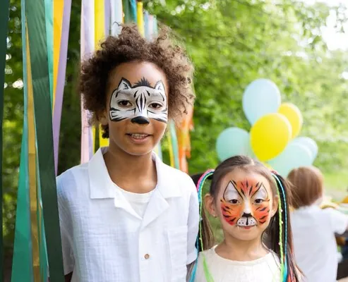 Two children with painted faces, a zebra and a tiger, at an outdoor party